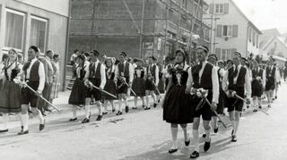 Eigentlich farbig, im Bild zeitbedingt schwarzweiß: Im Jahr 1960 stolz in der Langen Gasse unterwegs beim Herbstfestumzug – die roten und die grünen Tänzer. Ganz vorne die Gesichter heutiger Niederstettener Originale.