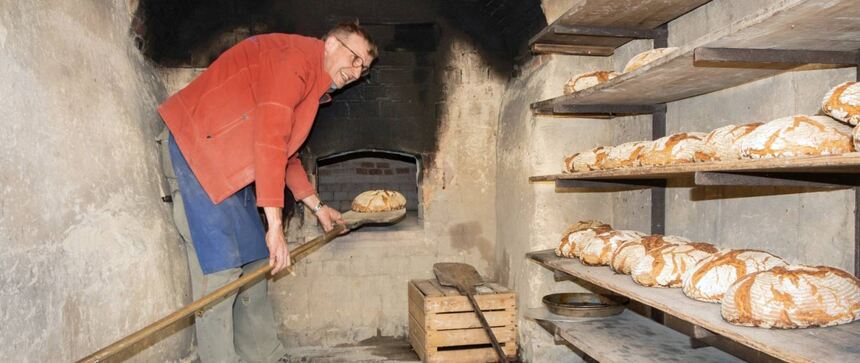 Der Bäcker holt mit der Brotschaufel fertige Brote aus dem Ofen.