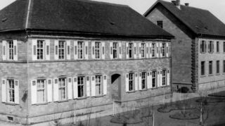 Die Aufnahme von Karl Weiß zeigt das im Jahr 1848 erbaute Schulgebäude und, im Bild rechts daneben, ein weiteres Schulgebäude, erbaut 1897. Unklar ist der Aufnahmezeitpunkt. Anlass könnte die 1904/05 erfolgte die Aufstockung auf sechs Klassen zu einem „Realprogymnasium“ gewesen sein.