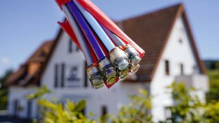 Ein Bündel mit Umhüllungen für Glasfaserkabel hängt auf einer Baustelle vor einem Wohnhaus.