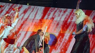 Jetzt wird’s bunt: In einer Parallelmontage lässt Regisseur Lars Wernecke zwei Szenen synchron laufen. Absoluter Hingucker ist dabei die Kussszene im Hintergrund – eine Scheibe macht Nähe möglich.