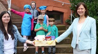 Erzieherin Samantha Griesfelder (links) überreicht im Beisein mehrerer Kinder der Kita „Schatzkiste“ eine Kochkiste inklusive eines Kochbuches an Boxbergs Bürgermeisterin Heidrun Beck (rechts).