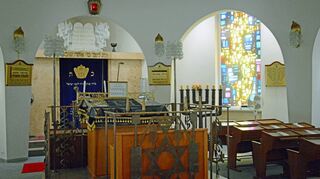 Blick in den Gottesdienstraum der Würzburger Synagoge: Im Hintergrund der Tora-Schrein (auch Heilige Lade), davor das Lesepult, oben ein Ewiges Licht, rechts die Menora, auch bekannt als Siebenarmiger Leuchter.