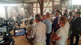Drehort Grünsfeld: Im historischen Rathaus spielt die Szene einer (film-)öffentlichen Gemeinderatssitzung. Am Tisch sitzend sind u.a. die bekannten Schauspieler Ulrich Tukur und Sebastian Bezzel (als Bürgermeister) zu erkennen.