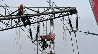 In luftiger Höhe werden die Stromleitungen unterhalb der Isolatoren am neuen Mast wieder befestigt.