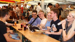 Gute Laune am Tisch im Festzelt. Im Hintergrund sieht man die Warteschlange an der Essensausgabe.
