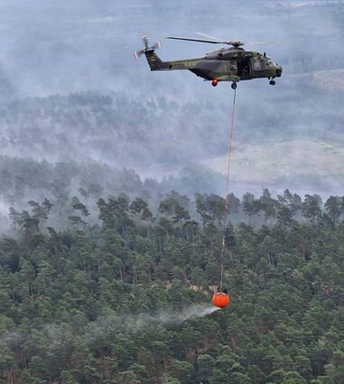 Ein NH90 mit gefüllten „Bambi Bucket“ fliegt die Stelle an, an der er die 2000 Liter Wasser gezielt abwirft.