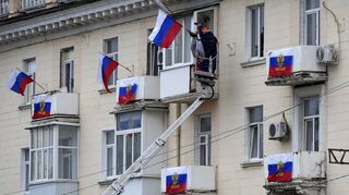 Arbeiter hängen russische Fahnen an einem Wohnhaus in der von Russland unterstützten Volksrepublik Luhansk auf.