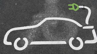 Ein Piktogramm eines Elektroautos ist auf einem Parkplatz an einer Ladestation auf dem Asphalt aufgemalt.