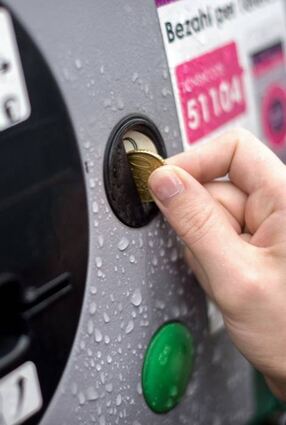 Geld wird in einen Parkscheinautomaten geworfen.