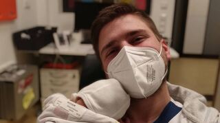 Das Glück, ein neugeborenes Baby im Arm zu halten, ist Kilian Lanig trotz Maske anzusehen.