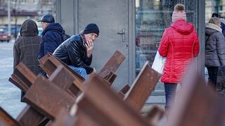 Passanten stehen an Panzersperren an einer Bushaltestelle in der ukrainischen Hauptstadt Kiew.
