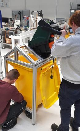 Am Häcksler für Verpackungsmüll arbeiten Calvilanus Shu Neba, Daniel Feller und Maurice Krämer.