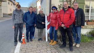 Hubert, Bernhard und Christine Steinbrenner, Doris Ebert, Meggi Steinbrenner, Ortsvorsteher Reinhard Belzner sowie Bernd Ebert (von links) zeigen anhand eines Pegelmessers, wie stark das Wasser 1993 in der Blumenstraße in Erlenbach angestiegen war: fast einen Meter hoch. Zahlreiche Häuser sind damals vollgelaufen.