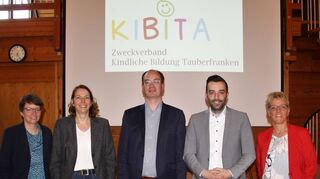 Konstituierende Sitzung mit (von links): Anja Günther (Lauda-Königshofen), Christina Häusler (Großrinderfeld), die beiden Bürgermeister Dr. Lukas Braun und Johannes Leibold sowie Sabine Baumeister (Schriftführerin) vor dem Logo des neuen Zweckverbandes „Kindliche Bildung Tauberfranken (Kibita)“. Nicht anwesend waren Frank Schönhöfer (Stellvertreter Lauda-Königshofen) und Julian Michelbach (Vertreter Großrinderfeld).