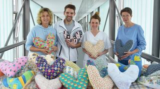 Carola Rollmann (rechts) hat die während der beiden vorherigen Nähaktionen entstandenen 300 Herzkissen nach Aalen gebracht. Stationsleiter Tobias Kinzl und seine Mitarbeiterinnen sind heilfroh, die liebevoll hergestellten Genesungshilfen ihren Patientinnen weiterschenken zu können.