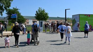 Besucher laufen am Eingangsbereich der Bundesgartenschau auf Spinelli. Viele beklagen den mangelnden Sonnenschutz auf dem Gelände.