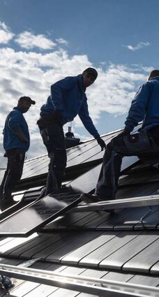 Mitarbeiter einer Fachfirma montieren Photovoltaikmodule auf dem Dach eines Hauses.