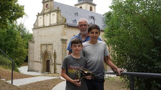 David, Johann und Harald Stuka (von vorne) präsentieren vor der Kulisse der Bergkirche ihren Fund.