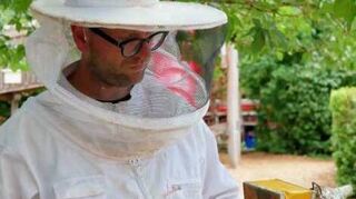 Tim Schnyder trägt Imkerschutzkleidung und hält in der Hand den „Smoker“.