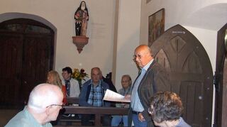 Egon Kirschner vom „Förderverein Katharinenkapelle Külsheim“ (stehend, rechts im Bild) erläutert vor Ort zur Statue der Edith Stein (hinten im Bild).
