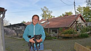 Das Tierheim unterhalb der Igersheimer Burg Neuhaus ist stark in die Jahre gekommen (Hintergrund) und soll 2025 aufgegeben werden. Ein Neubau am Bad Mergentheimer Stadtrand steht an. Um weitere Spenden wirbt die Vorsitzende des Tierschutzvereins Bad Mergentheim und Umgebung, Heidrun Leiss-Schott, die auf dem Bild mit Peppino zu sehen ist, einem vor sechs Wochen im Kurpark gefundenen Rehpinscher-Mix, dessen Herrchen unbekannt ist und der jetzt ein neues Zuhause sucht.