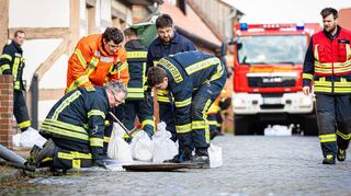 Einsatzkräfte der Feuerwehr dichten Kanaldeckel mit Folie und Sandsäcken ab.