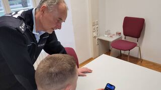 Olaf Bamberger, Leiter des Polizeireviers Bad Mergentheim, lässt sich das PoliPhone von einem Kollegen für dieses Symbolbild beispielhaft zeigen. Bislang sind alle Beamten im Streifendienst mit einem solchen Gerät ausgestattet, das die Arbeit schneller und effizienter gestalten soll.