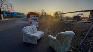 Eine abgewohnte Couchgarnitur steht bei Sonnenaufgang am Altkleidercontainer an der Pestalozziallee.