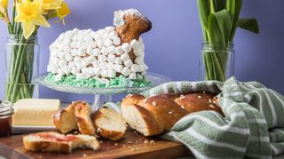 Das mit Marshmallows betupfte Osterlamm thront auf einer Wiese aus grün gefärbten Kokosraspeln. Davor lädt der angeschnittene Hefezopf zum Zugreifen ein.