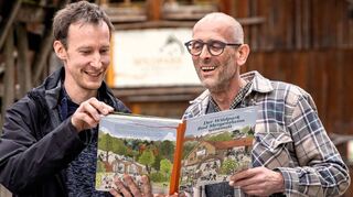 Der Zeichner, Illustrator und Cartoonist Hannes Mercker (links) sowie Geschäftsführer Marcus („Max“) Rügamer mit dem neuen Buch „Der Wildpark Bad Mergentheim wimmelt“, das zum 50-Jahr-Jubiläum des Wildparks erstellt wurde.