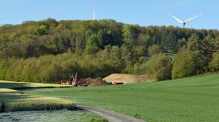 Vorne haben die Bauarbeiten am Waldrand begonnen; hinten drehen sich die Windräder nahe Bobstadt.