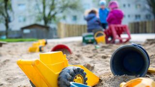 Spielzeug liegt in einem Sandkasten während die Kinder weiter hinten spielen.