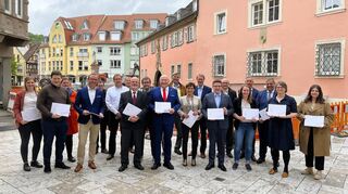 OB Udo Glatthaar (Mitte) überreichte vor der Kulisse des „Starterprojektes“ Gänsmarkt den Rahmenplan für die Landesgartenschau an Staatssekretärin Sabine Kurtz MdL (rechts neben ihm) und Ralph König (links von ihm) im Beisein von Landrat Christoph Schauder (Siebter von rechts) und weiteren Gästen sowie den „Gesichtern“ der Landesgartenschau Bad Mergentheim.