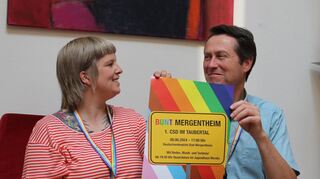 Verena Reichenberger und Robert Schiffmann gehören zum Bad Mergentheimer CSD-Orgateam. Das regenbogenbunte Plakat mit dem „Bunt Mergentheim“-Ortsschild fällt schon von weitem auf.