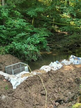 Der Bach wird für die Dauer der Bauarbeiten umgeleitet und über ein Rohr wieder in sein altes Flussbett „entlassen. Gut zu sehen ist auf dem rechten Bild noch die kleinere der beiden entstandenen Ausspülung hinter der zweiten Herdmauer.
