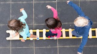 Kinder balancieren auf dem Spielplatz einer Kindertagesstätte auf einem Brett.