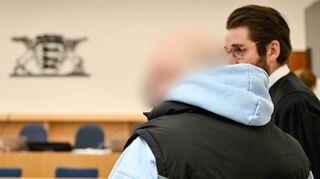 Einer der drei Angeklagten (l.) steht im Verhandlungssaal des Mannheimer Landgerichts vor der Richterbank.