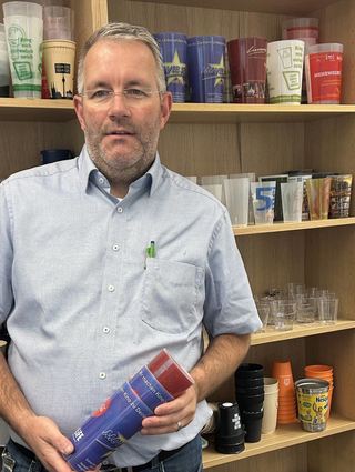 Sven Döding mit einer großen Mehrweg-Becherauswahl im Hintergrund.