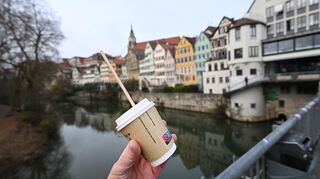 Eine Hand hält einen Einweg-Kaffeebecher vor dem Hintergrund der Tübinger Altstadt. Die Stadt Tübingen hat mit ihrer Verpackungssteuer den Anfang in Deutschland gemacht. Viele Kommunen, auch in der Region, wollen nun nachziehen.