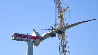 Winzig klein sind die Mitarbeiter auf dem Maschinenhaus zu erkennen, während eines der Rotorblätter montiert wird.