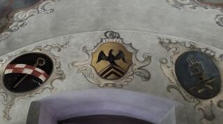 Die drei Medaillons zeigen die drei maßgeblichen Wappen: das rot-weiße schachbrettartige der Zisterzienser (links), das Wappen mit Adler von Abt Ambrosius Balbus (Mitte) und das Bronnbacher Wappen mit Dreischalenbrunnen (rechts).