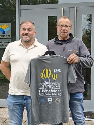 Ortsvorsteher Christian Stemmler (links) und Ballonfahrer Gerhard Weber haben mit der Planung des Cups alle Hände voll zu tun. Auch Merchandising gehört dazu - wie der Verkauf des extra angefertigten Shirts.
