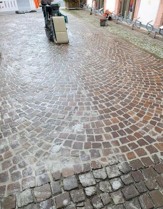Die Fugen im Marktplatz-Pflaster sind zunächst noch einmal ausgekehrt worden (im unteren Bereich zu sehen), bekamen dann eine Füllung und wurden maschinell abgewaschen. Das Testfeld befindet sich im Bereich Altes Rathaus/ Funkengasse.